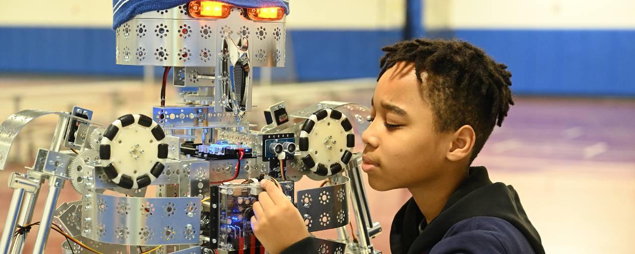 A boy works on a robot in a school classroom.